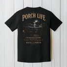 Black Comfort Colors porch life t-shirt displayed on a white wood background featuring dramatic lightning, mountain scenery, rocking chair, and Thunderstorms Are Better on the Porch artwork.