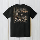 A black short-sleeve t-shirt shown from the back, featuring a large graphic print of two wolves in a forest with the text 'Pack Life' and 'Black Powder Apparel' printed below it. The shirt is displayed flat against a white vertical wood plank background.