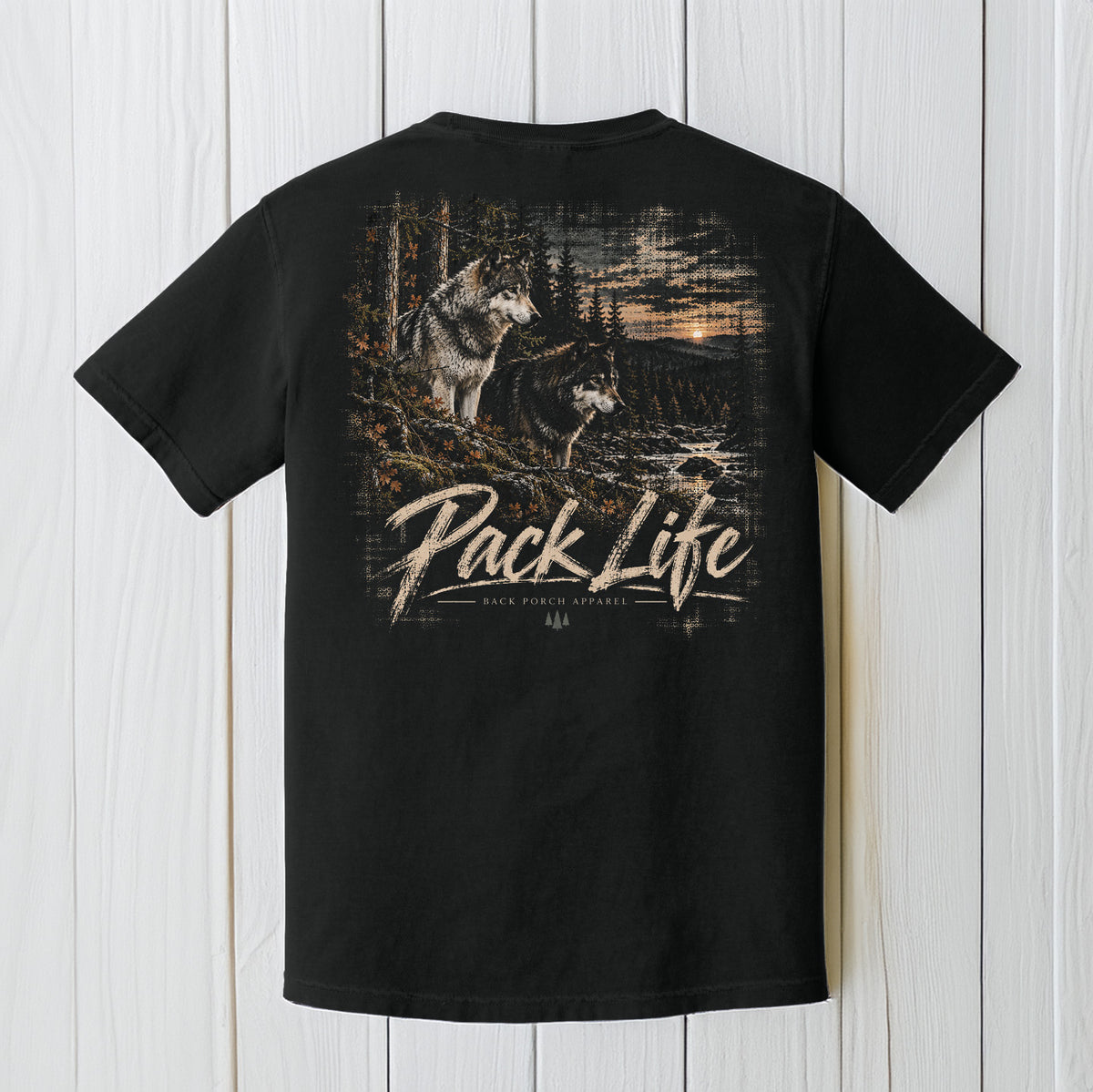 A black short-sleeve t-shirt shown from the back, featuring a large graphic print of two wolves in a forest with the text 'Pack Life' and 'Black Powder Apparel' printed below it. The shirt is displayed flat against a white vertical wood plank background.