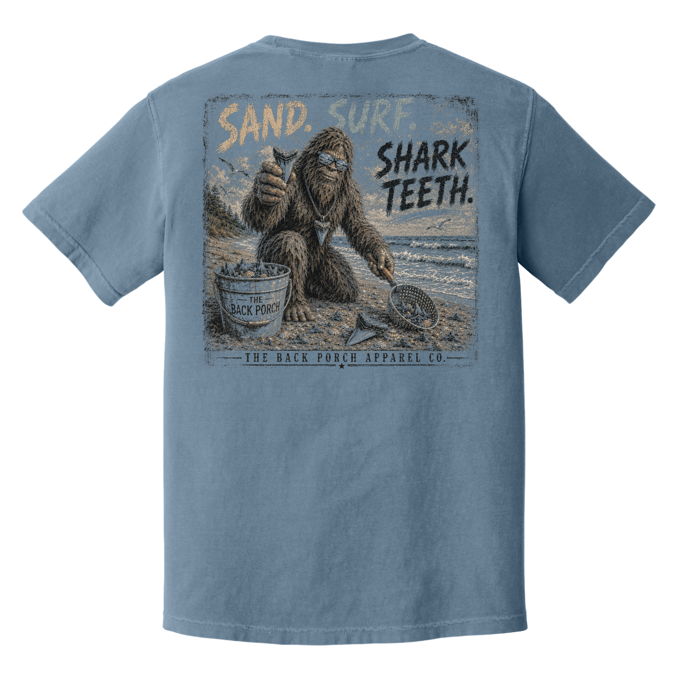 Back view of Back Porch Apparel Co. Sand. Surf. Shark Teeth. graphic tee on Comfort Colors Blue Jean shirt with distressed Bigfoot shark tooth hunting design.
