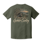 An olive green short-sleeve t-shirt shown from the back, featuring a large graphic print of a wild turkey in a forest landscape with the text 'Gobbler Country' in a distressed beige font.