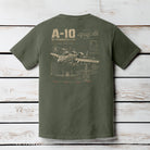 Moss Comfort Colors t-shirt hanging on a wood background featuring a distressed A-10 Thunderbolt II military aircraft schematic design.