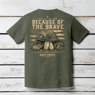 Moss Comfort Colors t-shirt hanging on a wood background featuring a distressed patriotic military graphic with tactical helmet and American flag artwork.
