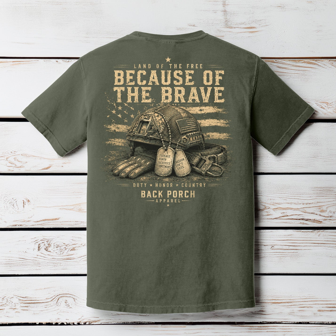 Moss Comfort Colors t-shirt hanging on a wood background featuring a distressed patriotic military graphic with tactical helmet and American flag artwork.