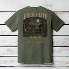 Moss Comfort Colors Porch Life graphic t-shirt displayed on a wood background featuring a peaceful porch scene with a full moon and glowing fireflies.