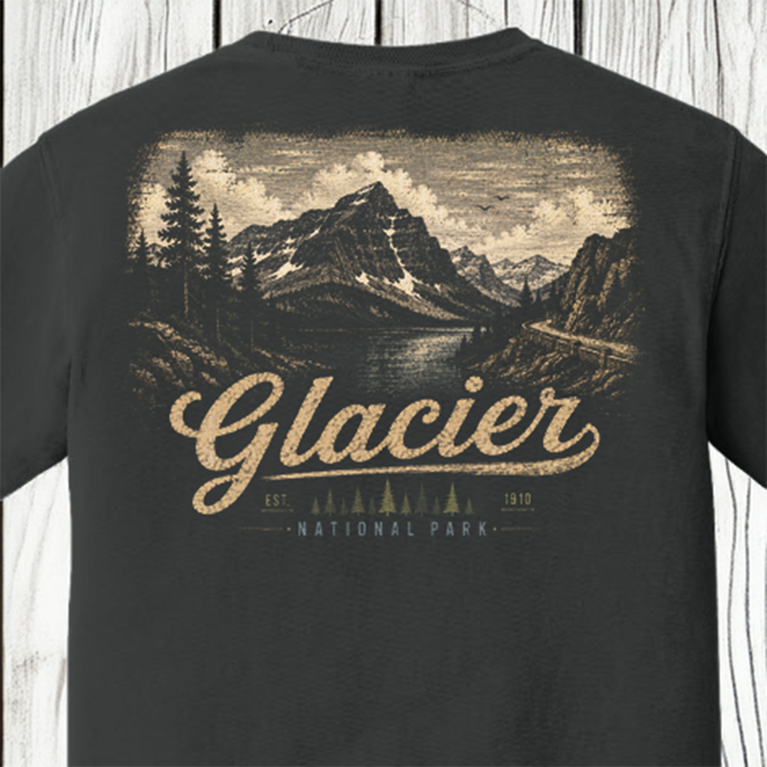 A dark charcoal gray t-shirt showing the back, which features a large vintage-style graphic of Glacier National Park with a mountain, lake, and pine trees in beige and brown tones, and the word 'Glacier' printed in large script.