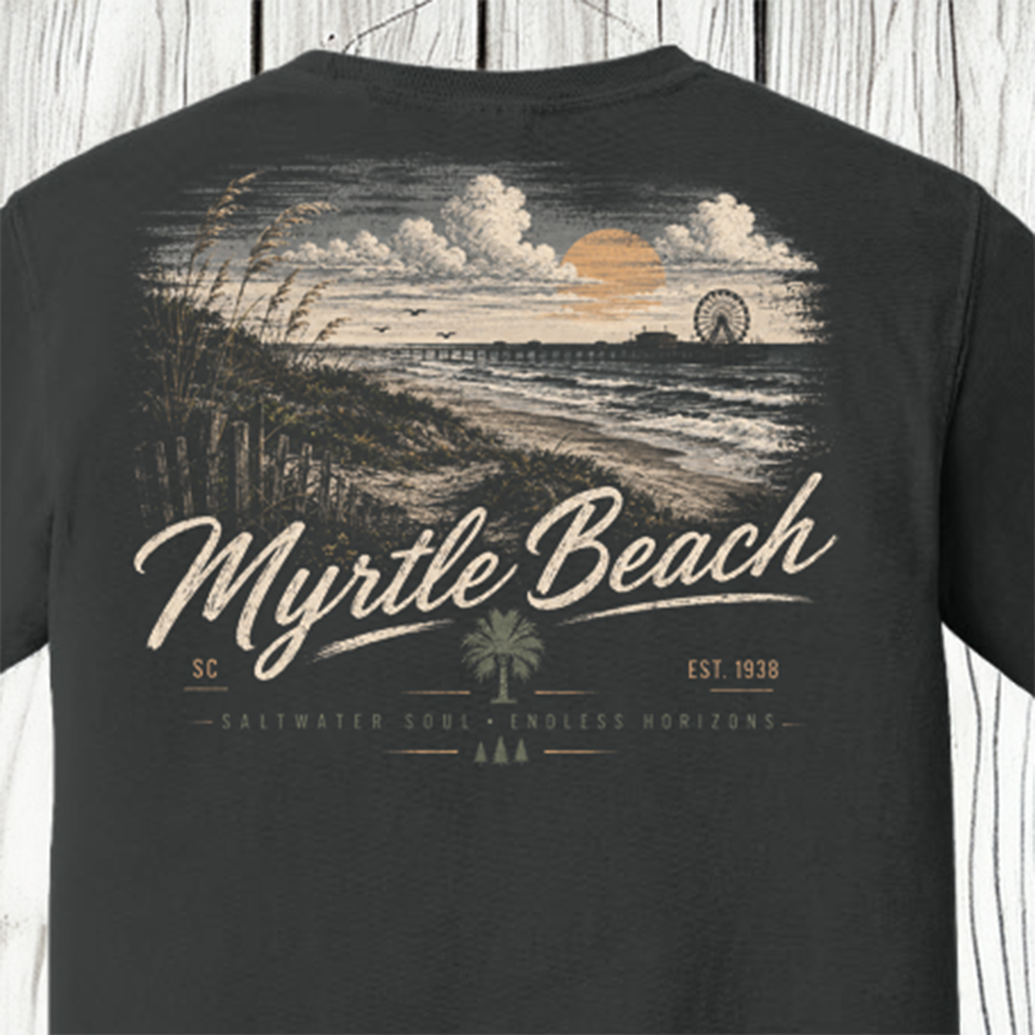 A dark charcoal gray t-shirt featuring a vintage-style graphic print of Myrtle Beach, SC. The design shows a beach sunset scene with a Ferris wheel, dunes, and a palm tree, with 'Myrtle Beach' written in large white script across the front.
