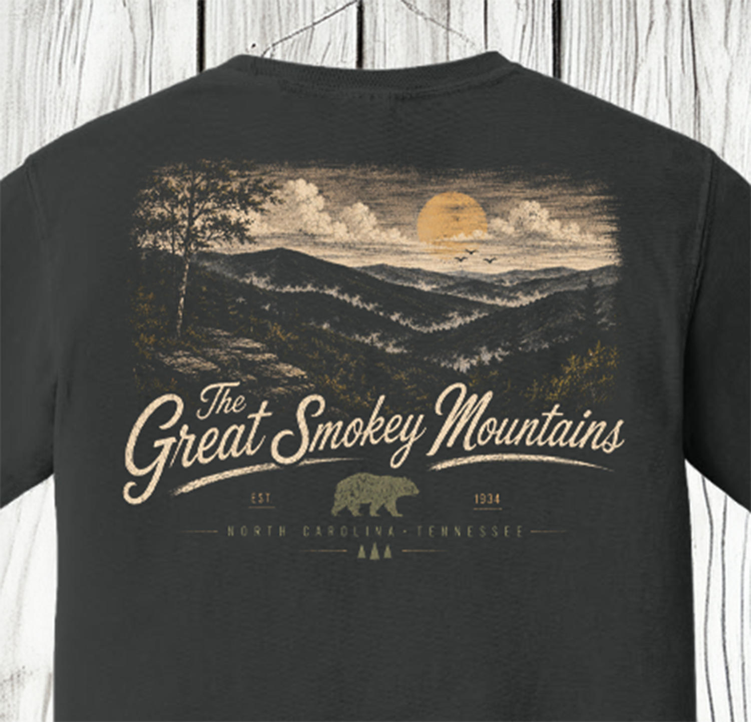A dark charcoal gray t-shirt featuring a vintage-style graphic print of the Great Smokey Mountains in North Carolina and Tennessee. The print depicts a bear, a bear cabin, and a large yellow moon over rolling mountains, with 'The Great Smokey Mountains' written in a cursive font.