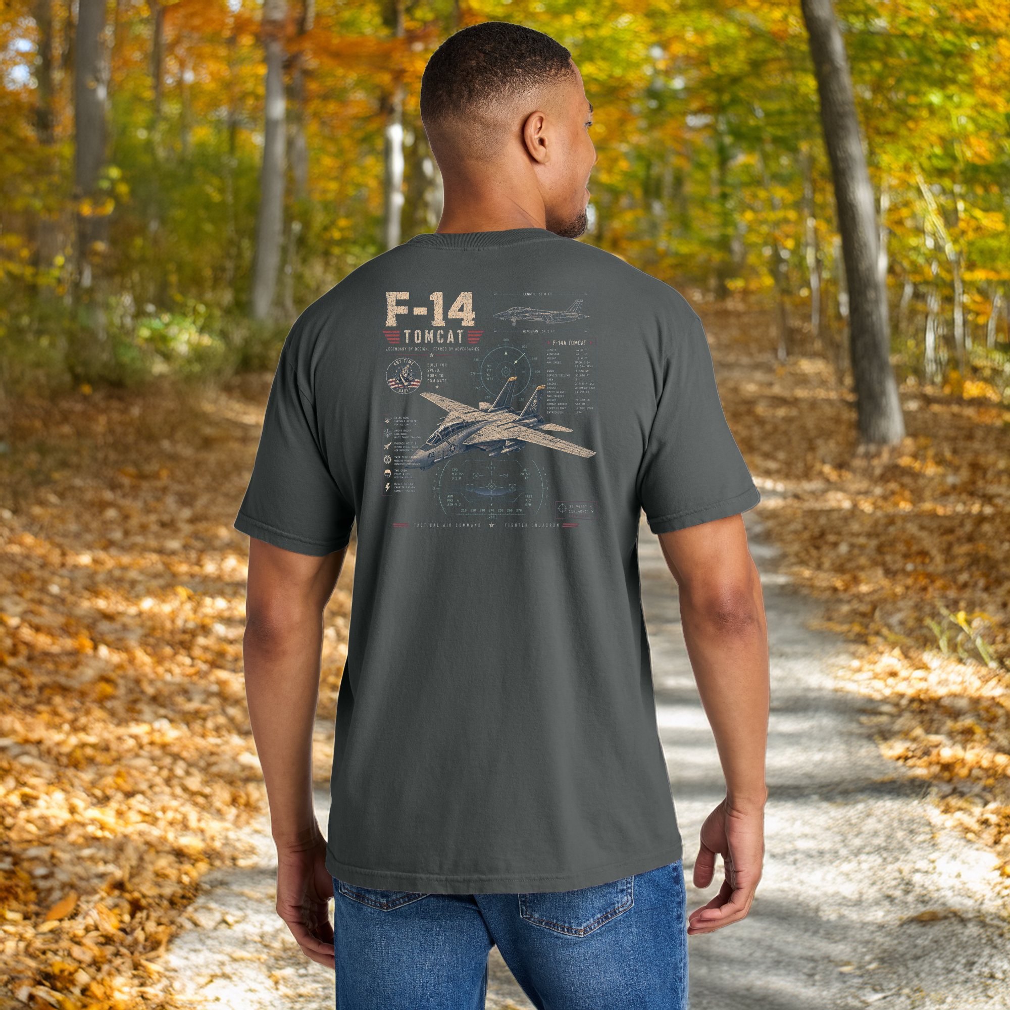 Model wearing a Comfort Colors Pepper t-shirt with a vintage F-14 Tomcat fighter jet graphic on the back while walking on a wooded trail.