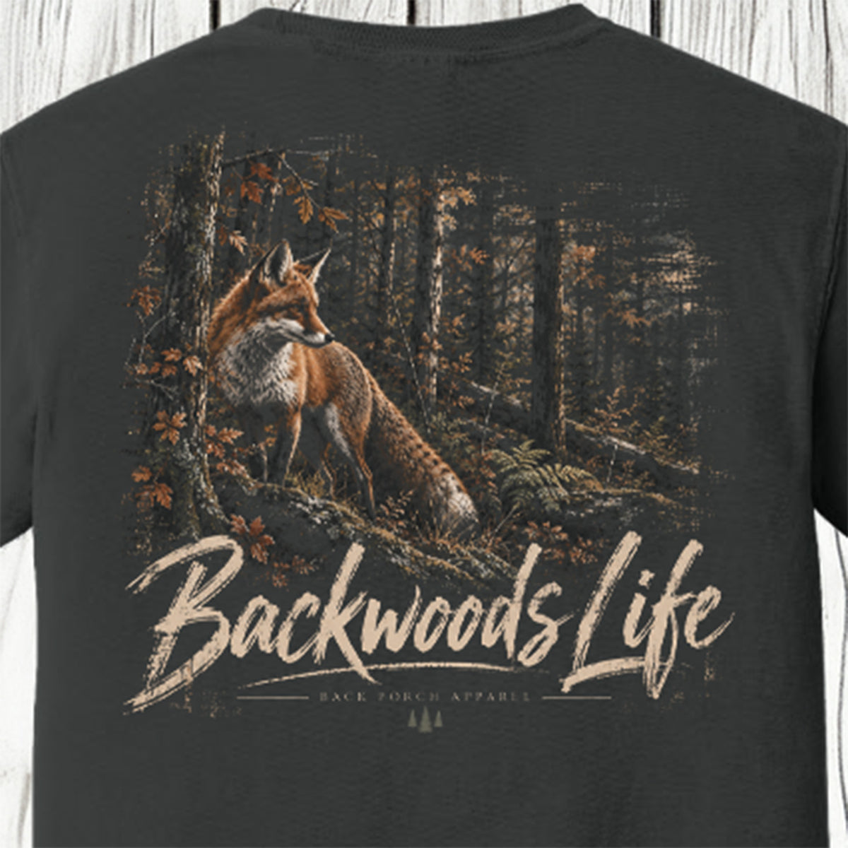 A dark charcoal gray t-shirt featuring a large graphic print of a red fox in a forest with the text 'Backwoods Life' and 'Back Porch Apparel' printed below it.