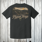 A dark charcoal gray t-shirt shown from the back, featuring a large vintage-style scenic graphic of a Tennessee mountain landscape with the text 'Pigeon Forge' and 'Tennessee 3616'. The shirt is displayed hanging against a light gray wood plank background.