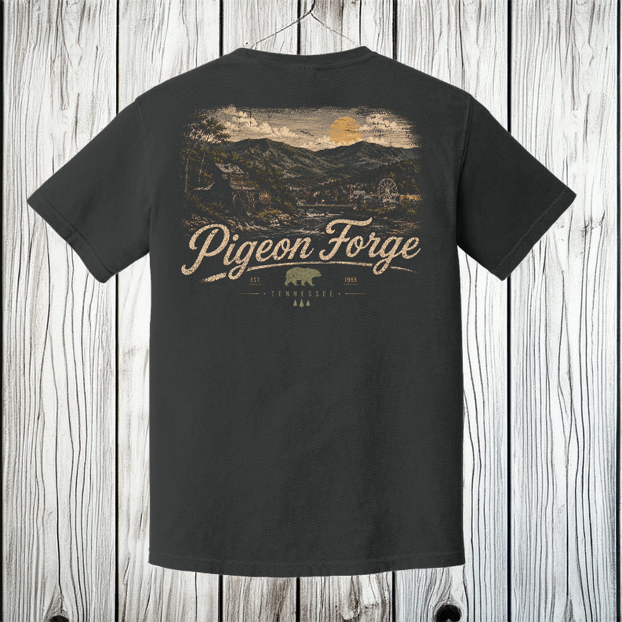 A dark charcoal gray t-shirt shown from the back, featuring a large vintage-style scenic graphic of a Tennessee mountain landscape with the text 'Pigeon Forge' and 'Tennessee 3616'. The shirt is displayed hanging against a light gray wood plank background.