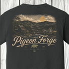 A dark charcoal gray t-shirt shown from the back, featuring a large vintage-style graphic print of a Tennessee landscape with mountains, a river, and a sun, with the text 'Pigeon Forge' and 'TENNESSEE' printed below.