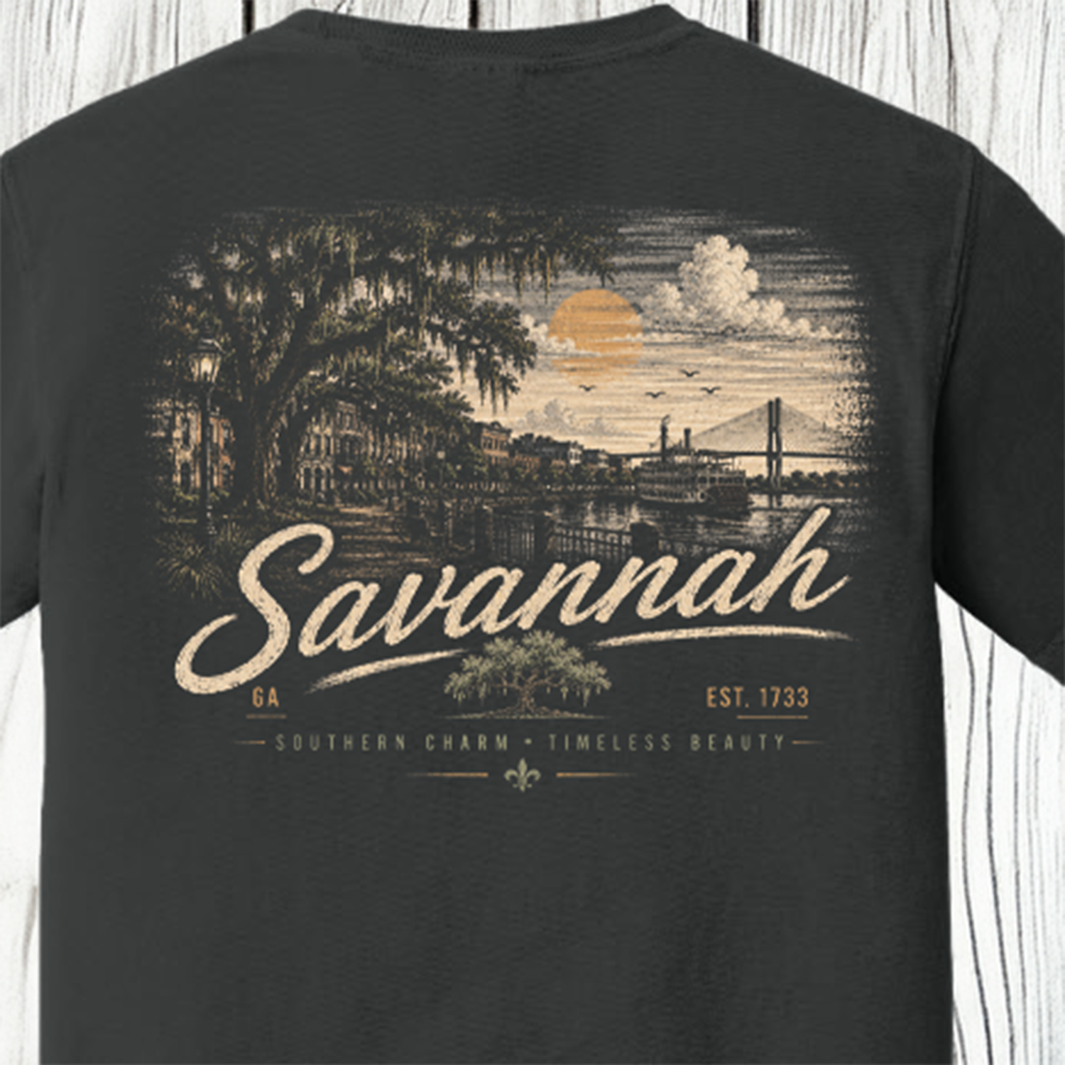 A dark charcoal gray t-shirt showing the back, which features a large vintage-style graphic print of Savannah, Georgia. The print depicts a scenic sunset over the city with a bridge, trees, and the word 'Savannah' in a large cream-colored script font.