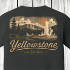 A dark charcoal gray t-shirt featuring a vintage-style Yellowstone National Park graphic on the front. The graphic depicts a geyser erupting from a mountain under a large orange sun, with 'Yellowstone' and 'National Park' written in a distressed beige font below.