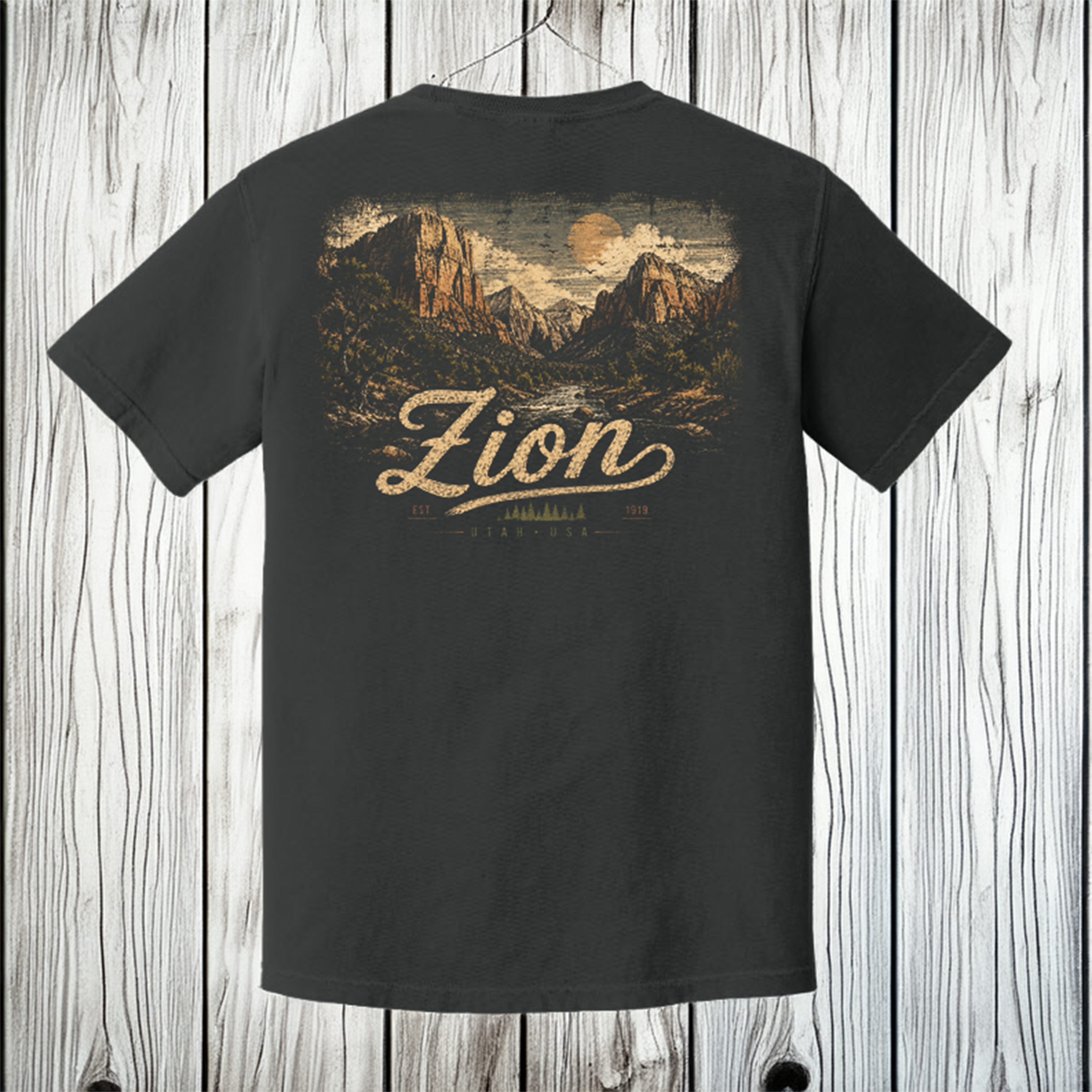 A dark charcoal gray t-shirt shown from the back, featuring a vintage-style graphic of Zion National Park with the word 'Zion' in a large cursive font. The t-shirt is displayed hanging against a rustic white-washed wooden plank background.