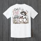 White unisex t-shirt featuring a "Can I Pet That Dog" graphic with a smiling blue-eyed husky puppy peeking over a rustic wooden fence, displayed on a wood background.