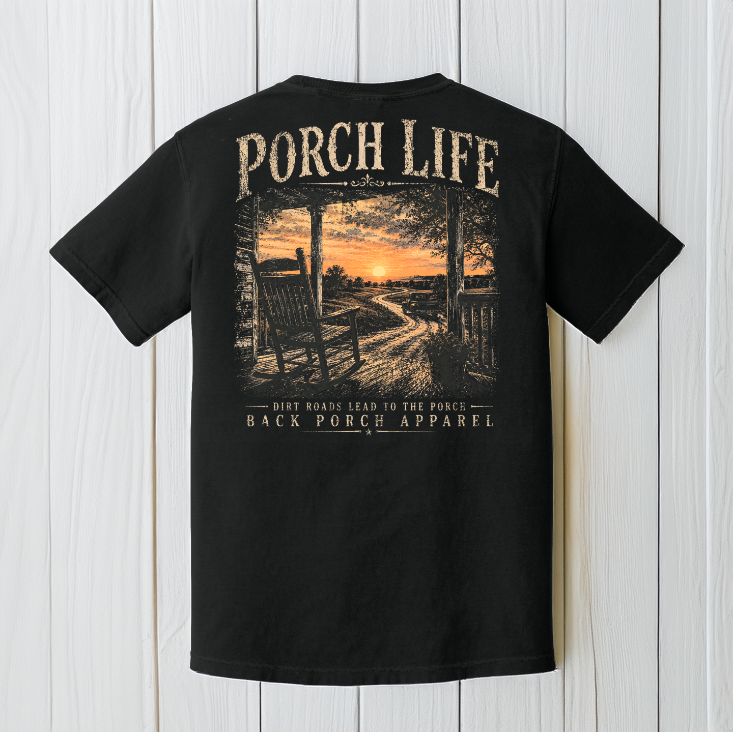 Black Comfort Colors Porch Life graphic t-shirt displayed against a rustic wood background featuring a peaceful country porch at sunset.