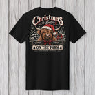 A black short-sleeve t-shirt displayed flat against a light gray wood plank background, showing the back graphic. The graphic features a Highland cow in a red Santa hat and plaid bow tie, with the text 'Christmas is Better ON THE FARM' and 'BLACK DOGS APPAREL' printed below.