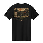 A black short-sleeve t-shirt shown from the back, featuring a large vintage-style graphic print of a Pennsylvania landscape with a sunset, bridge, trees, and the word 'Pennsylvania' in tan and orange lettering.