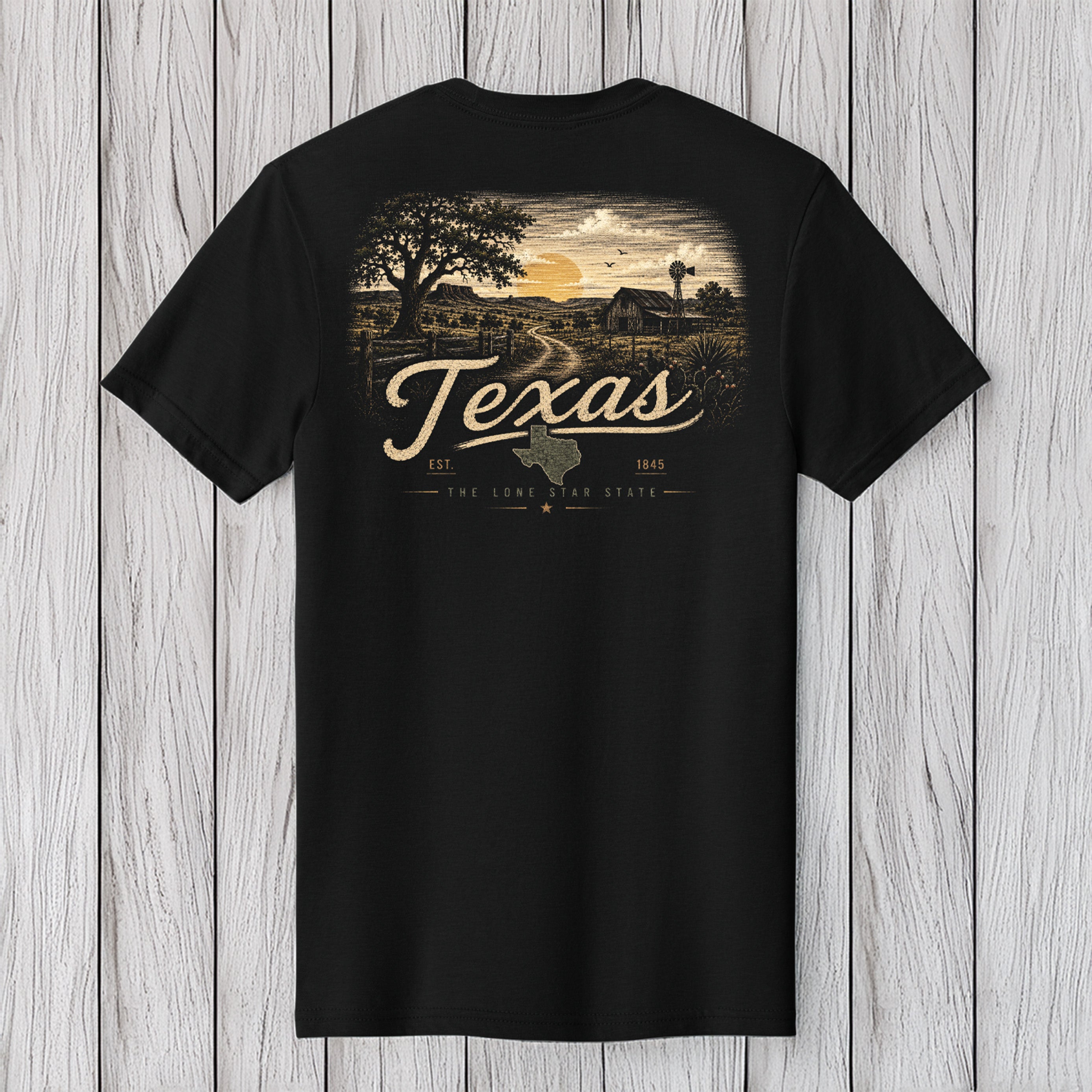 A black short-sleeve t-shirt with a vintage-style Texas landscape graphic on the front, featuring a sunset, trees, a barn, and the word 'Texas' in large script, displayed against a light gray wood plank background.