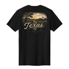 A black short-sleeve t-shirt shown from the back, featuring a large vintage-style graphic print of a Texas landscape with a sunset, barn, windmill, and the word 'Texas' in cream lettering.