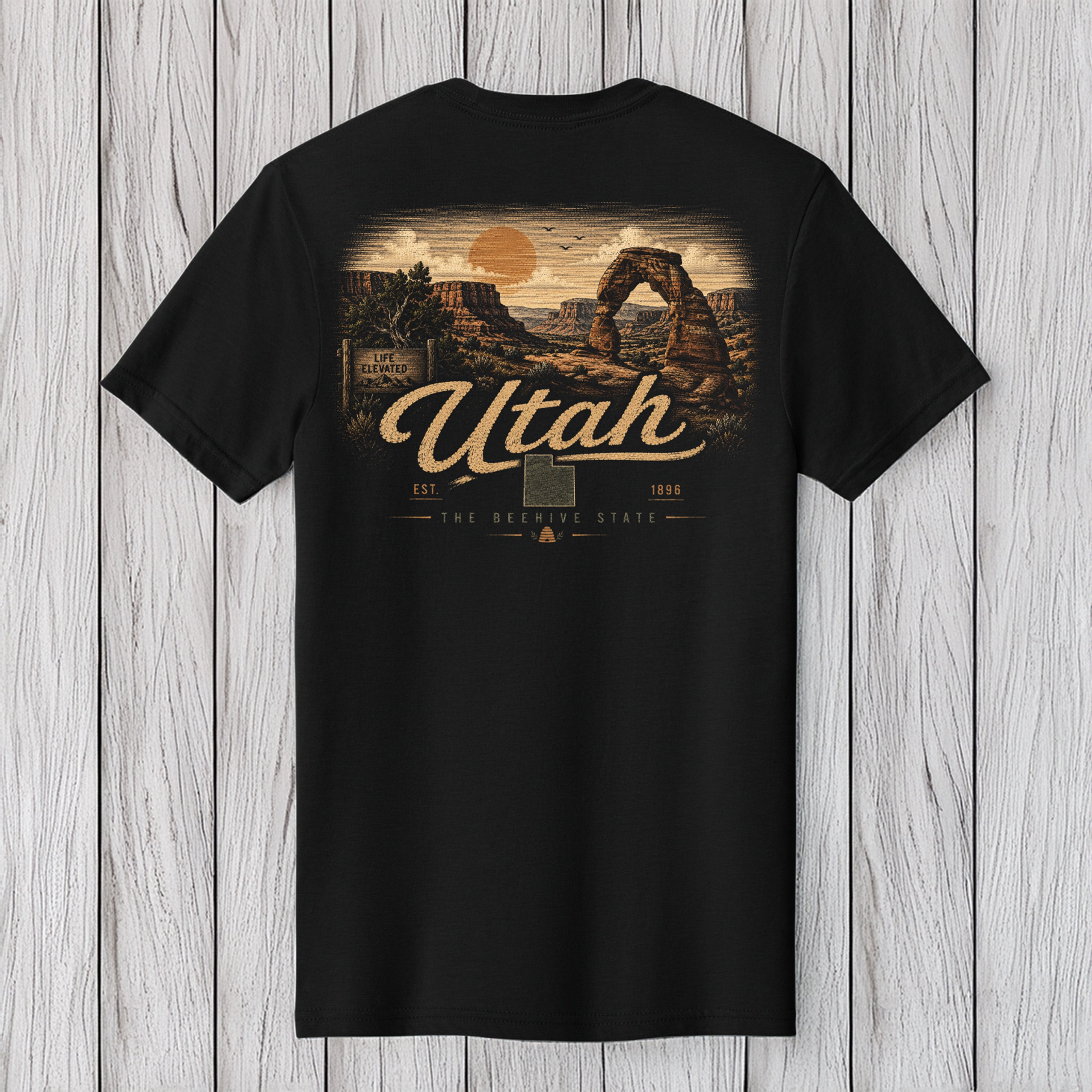 A black short-sleeve t-shirt with a vintage-style Utah graphic print on the front, displayed flat against a light gray wood plank background.