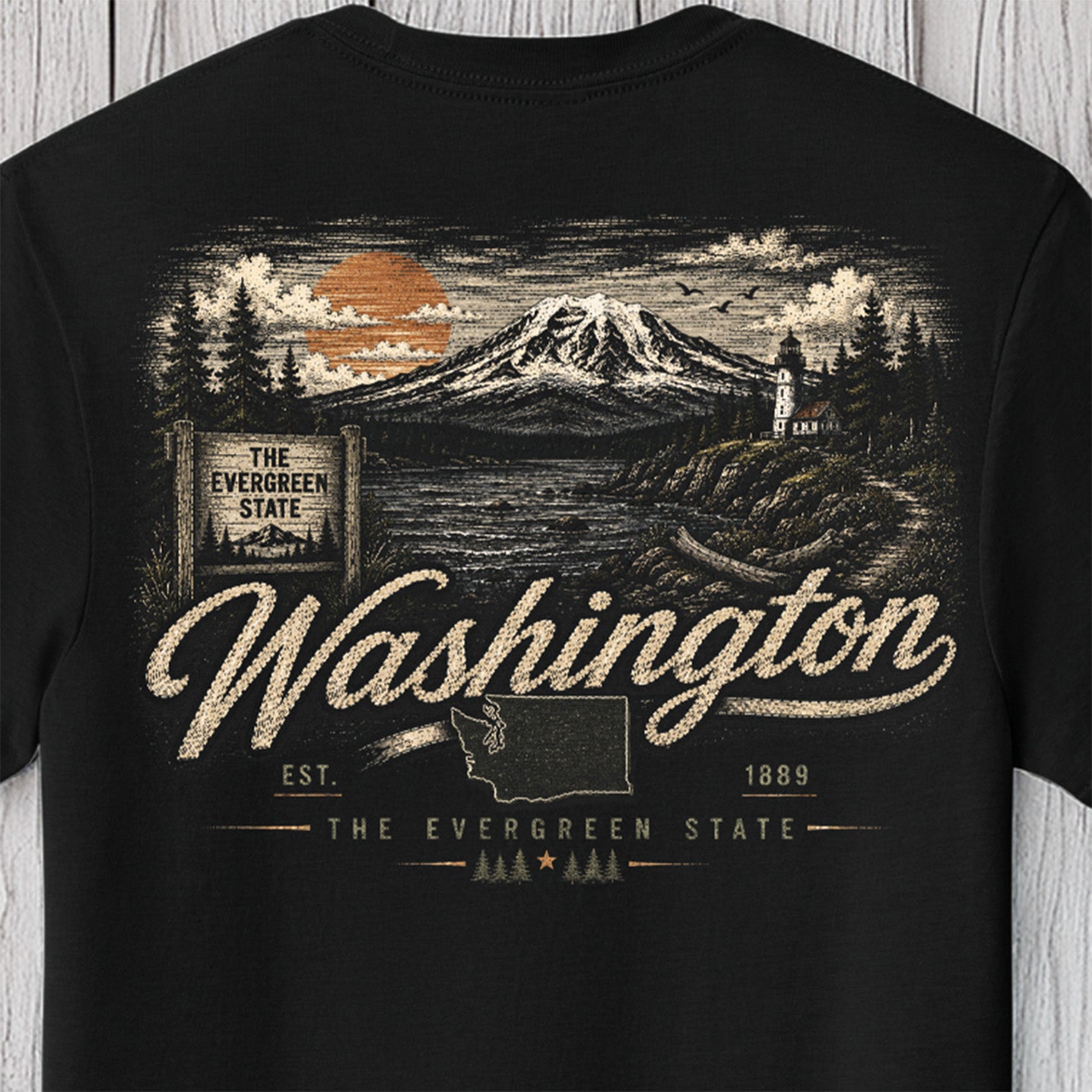 A black short-sleeve t-shirt featuring a detailed back graphic of Mount Hood, Oregon, with the text 'The Evergreen State' and 'Washington'. The design includes an orange sun, pine trees, a lighthouse, and a map outline of Washington, shown against a light gray wood plank background.