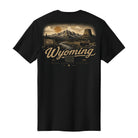 A black short-sleeve t-shirt with a detailed vintage-style Wyoming graphic on the front, featuring a mountain landscape, a sunset, and the text 'Wyoming' in a cursive font.