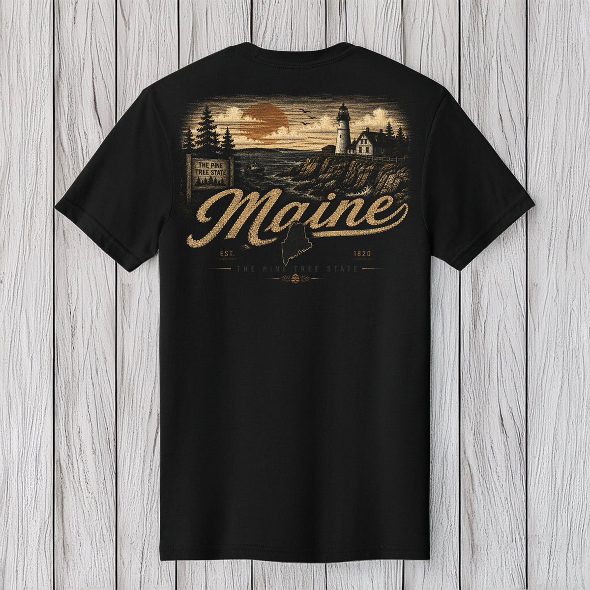 A black short-sleeve t-shirt with a vintage-style Maine graphic on the back, featuring a lighthouse, sunset, and the word 'Maine' in large script, displayed against a white wood plank background.