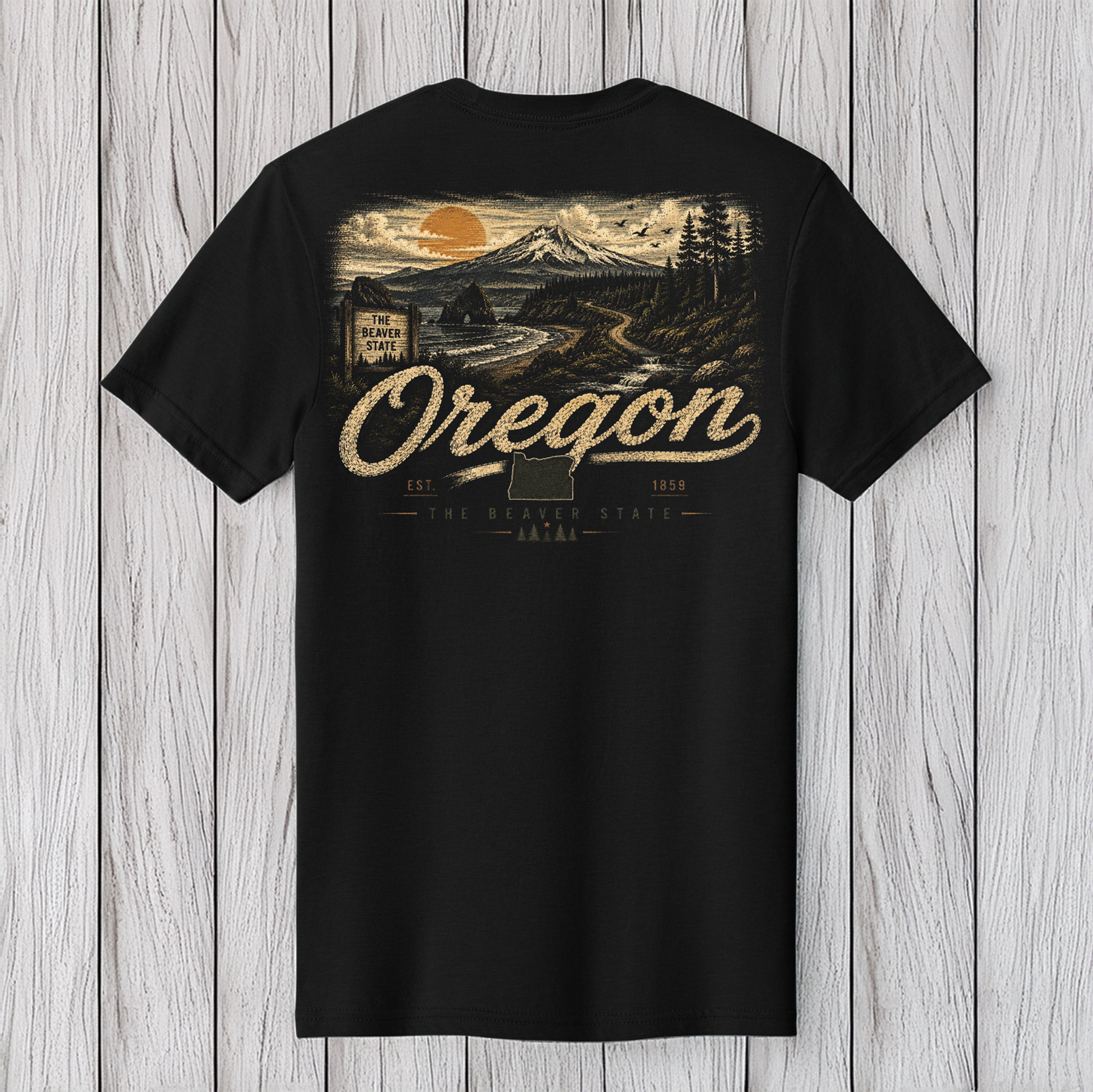 A black short-sleeve t-shirt with a large vintage-style Oregon graphic on the front, featuring a mountain, sunset, and the word 'Oregon' in beige, displayed against a light gray wood plank background.