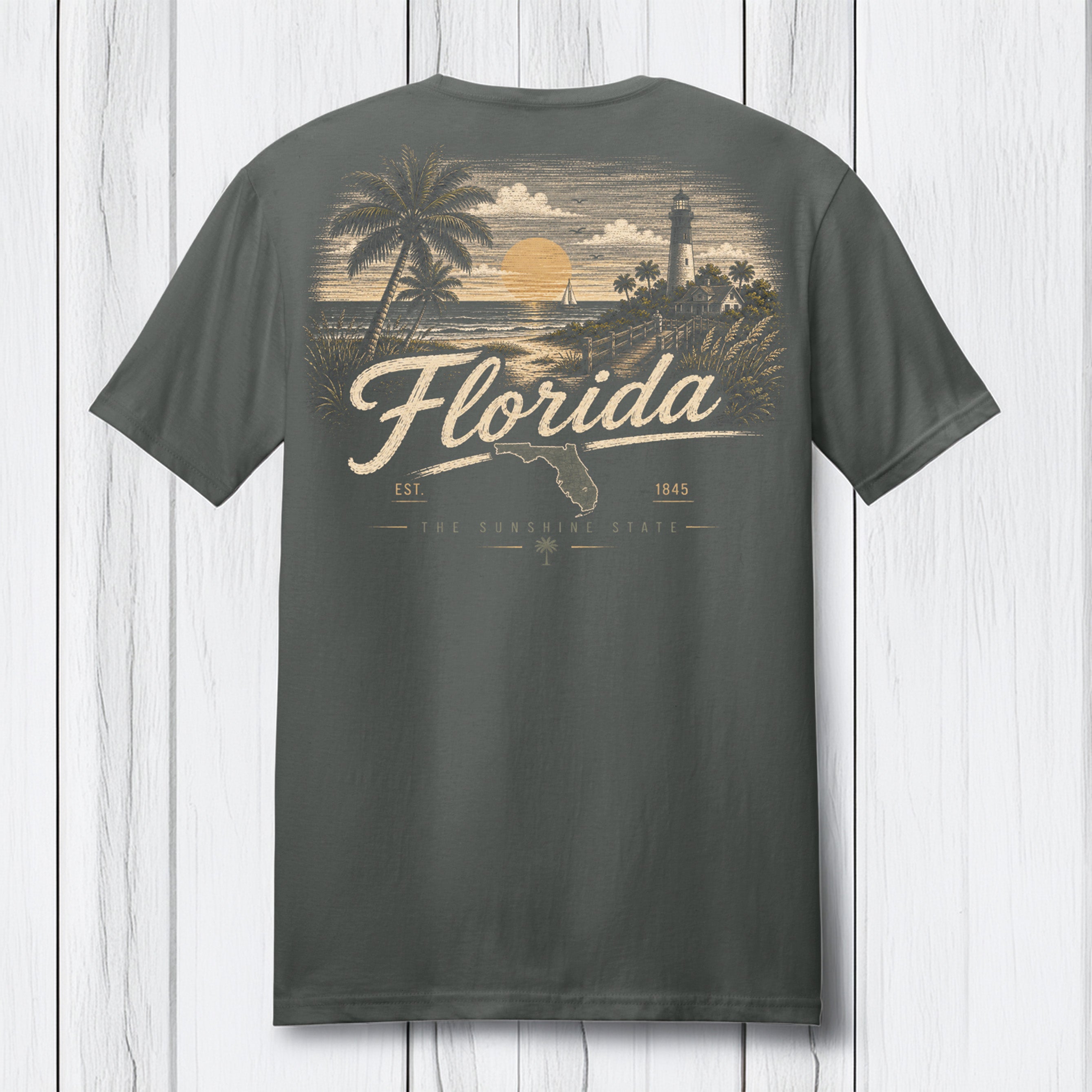 A dark gray t-shirt shown from the back, featuring a vintage-style Florida graphic print in beige and yellow tones with palm trees, a lighthouse, and the word 'Florida' in script, set against a white wood plank background.