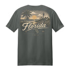 A dark gray t-shirt shown from the back, featuring a vintage-style graphic print of a Florida beach scene with palm trees, a lighthouse, and a sunset, with 'Florida' written in large script.