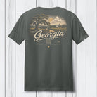 A dark gray t-shirt shown from the back, featuring a vintage-style graphic of a Georgia landscape with a tree, country road, and clouds, with 'Georgia' written in script across the center.