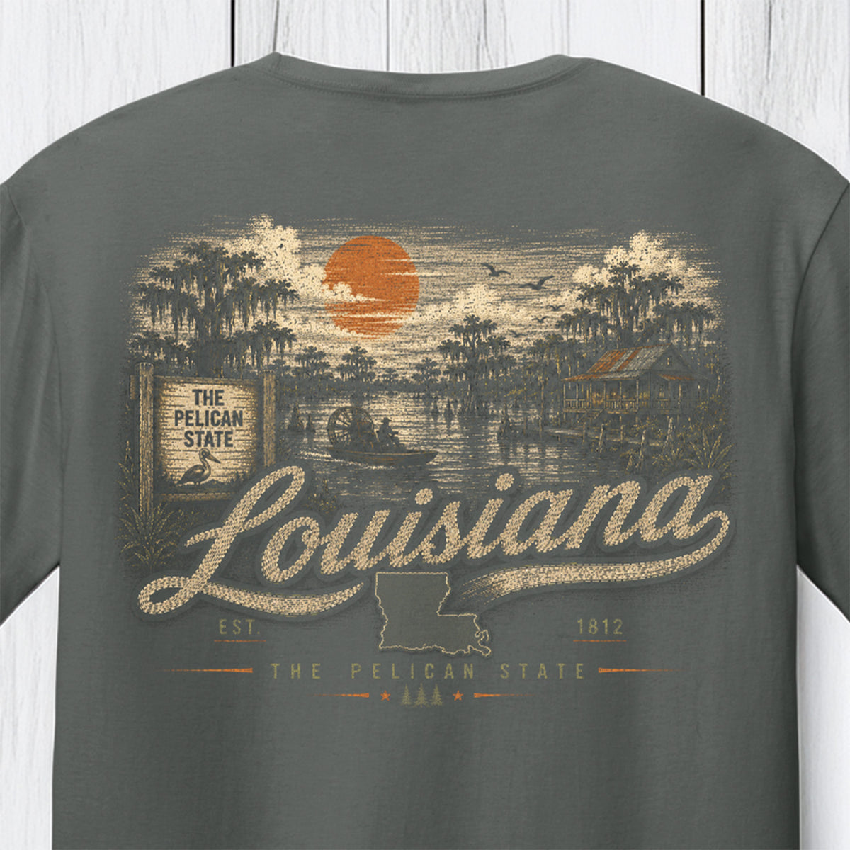 A dark gray crewneck t-shirt featuring a vintage-style Louisiana graphic print on the front. The design includes an orange sun, a swamp scene with trees, a duck, and the words 'The Pelican State' and 'Louisiana' in distressed lettering.
