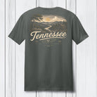 A dark gray t-shirt shown from the back, featuring a vintage-style Tennessee landscape graphic with a sunset, mountains, and a cabin, with 'Tennessee' printed in a large cream script.