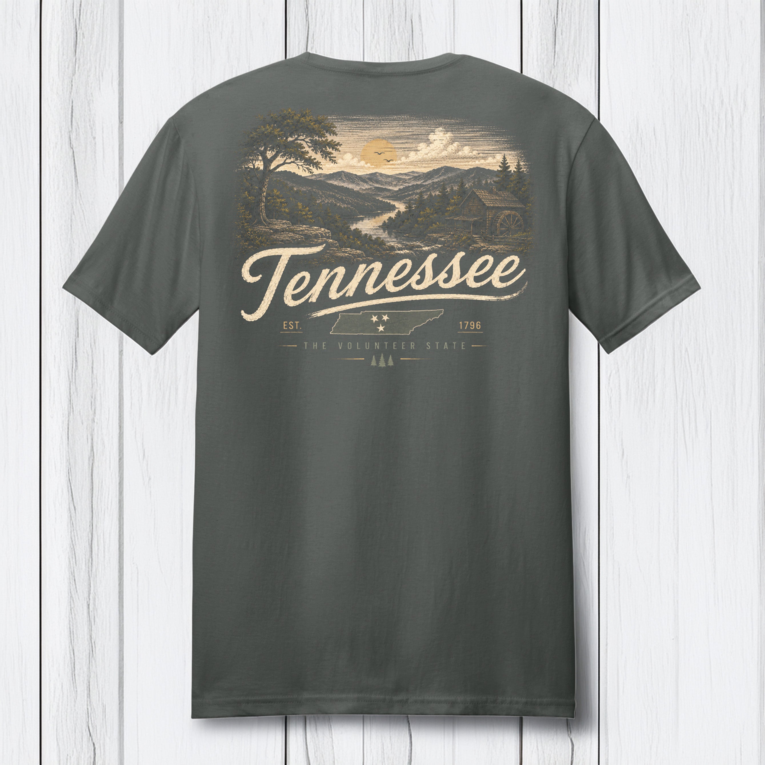A dark gray t-shirt shown from the back, featuring a vintage-style Tennessee landscape graphic with a sunset, mountains, and a cabin, with 'Tennessee' printed in a large cream script.