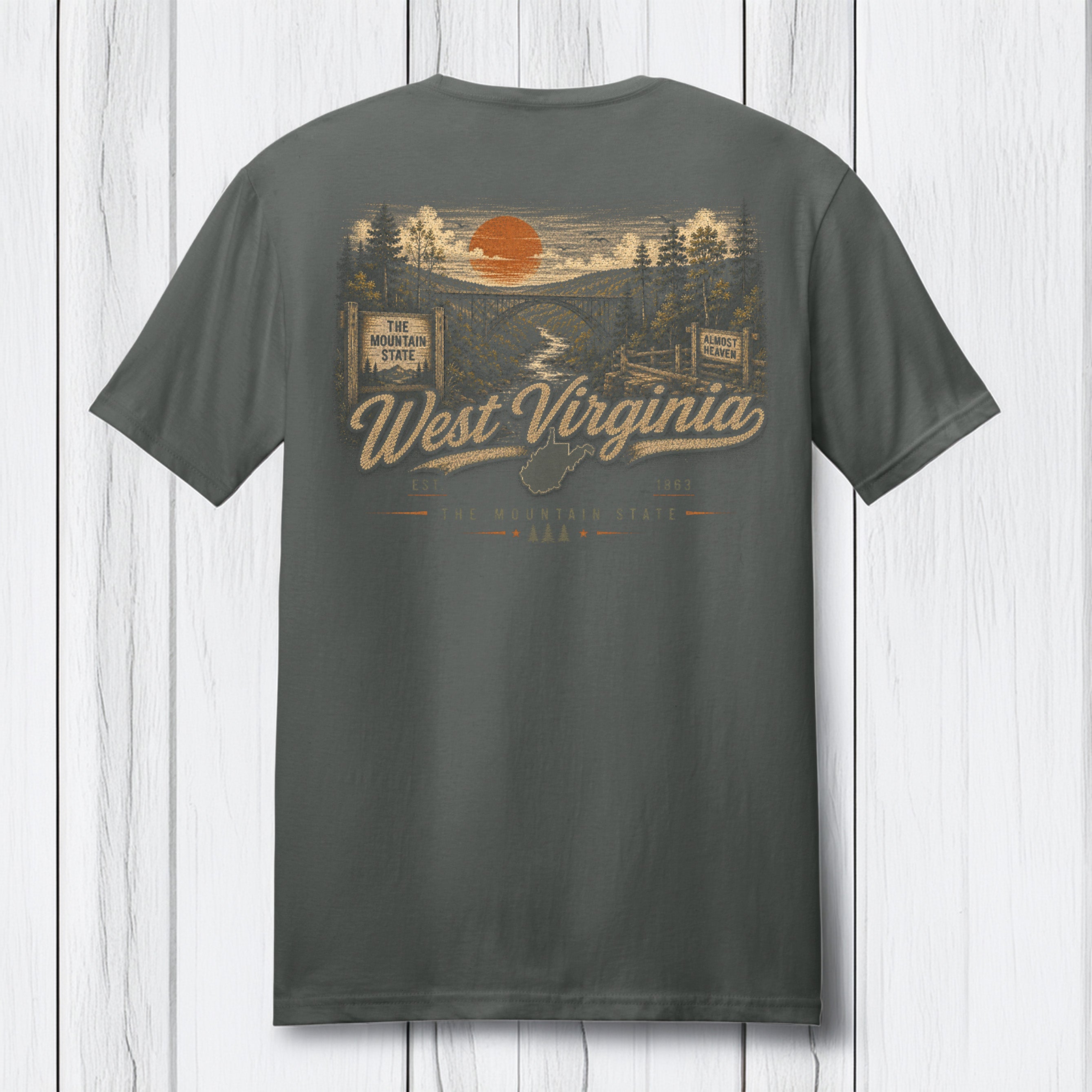 A dark gray t-shirt shown from the back, featuring a vintage-style West Virginia graphic with an orange sun, river, bridge, and 'West Virginia' text, displayed against a white wood plank background.