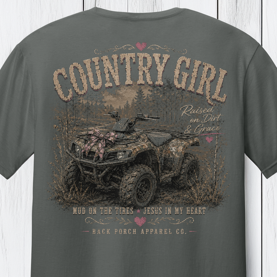 Distressed southern country girl graphic featuring a camouflage ATV, rustic woodland background, pink bow accents, and “Raised on Dirt & Grace” typography on a Comfort Colors shirt.