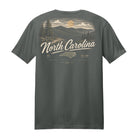 A dark gray short-sleeve t-shirt showing the back graphic, which features a scenic North Carolina landscape with mountains, pine trees, a sun, and the text 'North Carolina' in a cream-colored script.