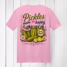 Pink 100% ring-spun cotton t-shirt featuring the "Pickles Make Me Happy" graphic with rustic pickle jars, smiling pickle slices, flowers, and Back Porch Apparel branding displayed on a white wood background.