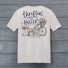 Close-up of the Thriftin' Through the Holler design featuring a vintage bicycle, antique books, flowers, flea market treasures, and rustic farmhouse artwork.