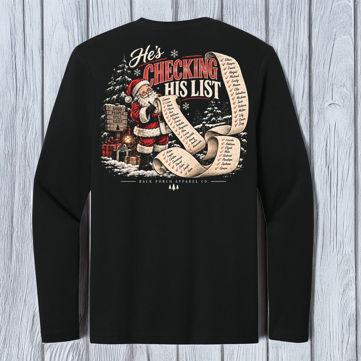A black long-sleeve t-shirt with a large Christmas graphic on the back, featuring Santa Claus and the text 'He's CHECKING HIS LIST' on a light gray wood plank background.