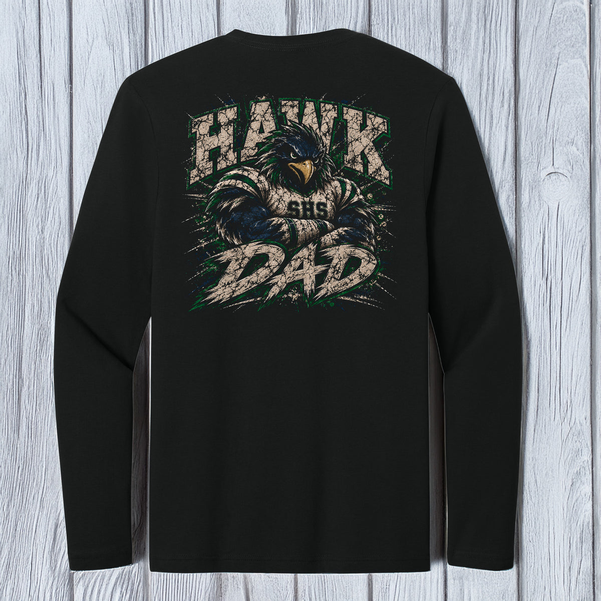 A black long-sleeve t-shirt with a large back graphic featuring a hawk and the words 'HAWK AND DAD' in distressed beige and green lettering, displayed against a light gray wood plank background.