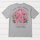 A light gray short-sleeve t-shirt shown from the back, featuring a large pink breast cancer awareness graphic with a pink ribbon, flowers, and the words 'FAITH HOPE STRENGTH' and 'Stronger TOGETHER' on a white wood plank background.