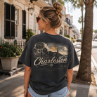 A woman wearing a charcoal gray graphic t-shirt with a vintage Charleston print, standing on a sunny city street.