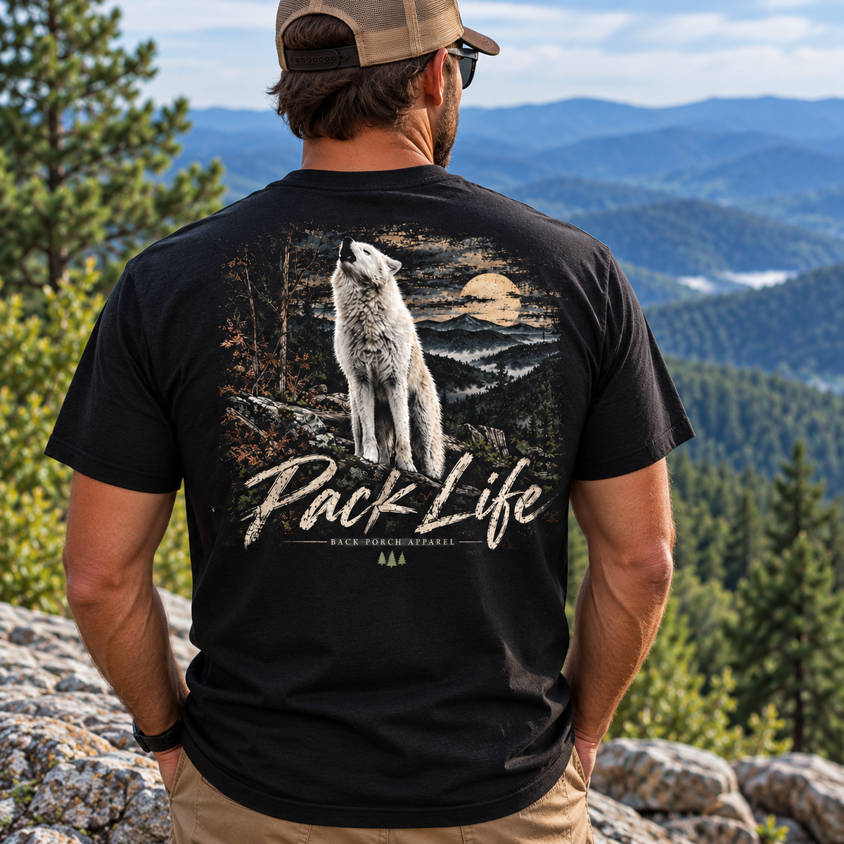 A man wearing a black graphic t-shirt with a large back print of a howling wolf and the text 'Pack Life', photographed from behind against a mountain landscape.