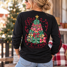 Woman wearing a black Simply Southern Christmas long sleeve shirt featuring a colorful Christmas tree made of festive bows and ribbons.