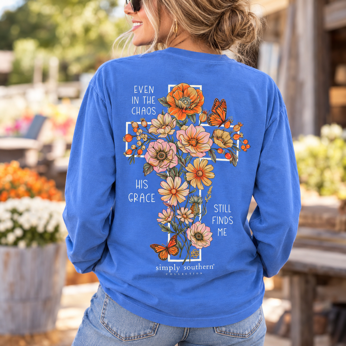 Woman wearing a blue Simply Southern His Grace long sleeve shirt with floral cross, orange butterflies and inspirational Christian message on the back.