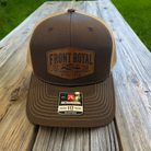 Front Royal Virginia leather patch Richardson 112 trucker hat standing on a rustic wooden picnic table with a blurred green outdoor background.